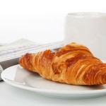 Zeitung, Tasse und Croissant