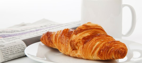 Zeitung, Tasse und Croissant